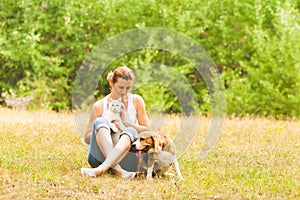 Smiling woman sitting on a grass with cat and dog