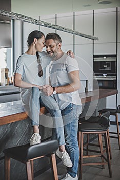 smiling woman sitting on kitchen counter and embracing boyfriend