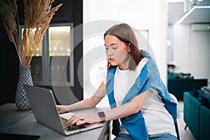 Smiling woman sitting in the kitchen and using the laptop. Working from home in quarantine lockdown. Social distancing