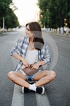 Smiling woman sitting in the middle of an empty city road, hand in fanny pack