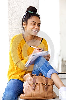 Smiling woman sitting outdoors and writing book