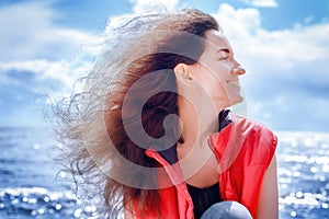 Smiling woman sitting by the sea with long curly hair flying in the wind