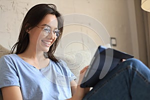 Smiling woman sitting on sofa with digital tablet and chating with friends