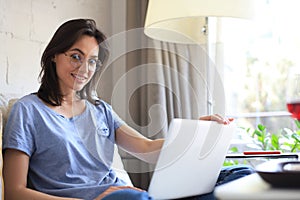 Smiling woman sitting on sofa with laptop computer and chating with friends