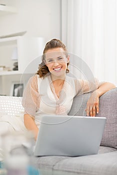 Smiling woman sitting on sofa in living room with laptop