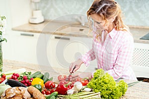 Smiling woman is slicing tomatoes on a kitchen table