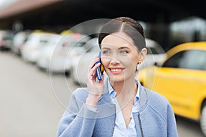 Smiling woman with smartphone over taxi in city