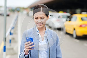 Smiling woman with smartphone over taxi in city