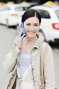 Smiling woman with smartphone over taxi in city