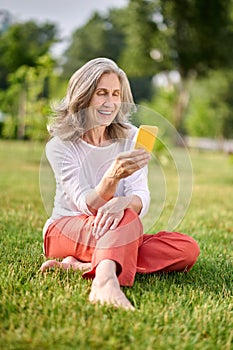 Smiling woman with smartphone sitting on grass