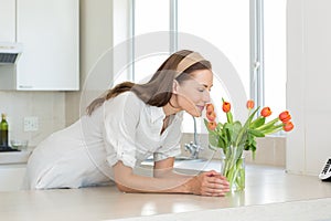 Smiling woman smelling flowers in kitchen