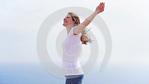 Smiling woman spining at cliff against blue sea. Carefree female traveleer dancing in slow motion