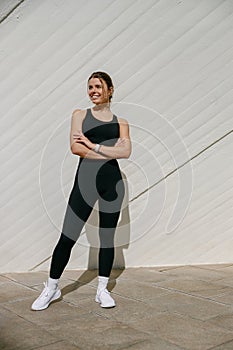 Smiling woman in sportswear have rest after workout outside standing on building background