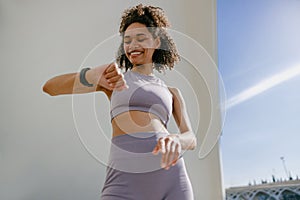 Smiling woman in sportswear looking on smartwatch after training. Outdoor sports in the morning