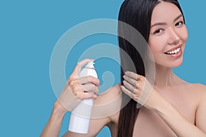 Smiling woman spraying new hairspray on her hair