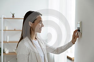 Smiling woman adjusting degrees set comfortable temperature using thermostat photo