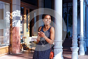 Smiling woman standing outside with earphones and mobile phone