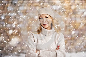 Smiling woman standing outside when snowing and wearing knit beanie and turtleneck sweater
