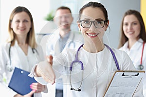 Smiling woman stretches out her hand for handshake behind her team of doctors