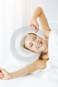 Smiling woman stretching hands in bed after waking up, entering a day happy and relaxed. Sweet dreams, sunny morning