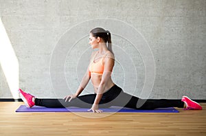 Smiling woman stretching leg on mat in gym