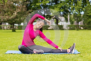 Smiling woman stretching leg on mat outdoors