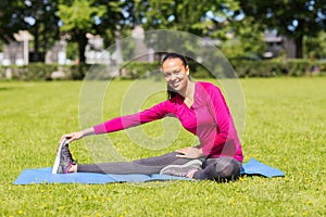 Smiling woman stretching leg on mat outdoors