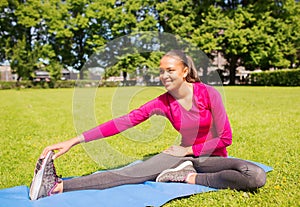 Smiling woman stretching leg on mat outdoors