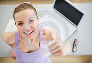 Smiling woman studying in kitchen and showing thumbs up