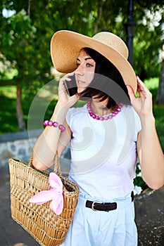 Smiling Woman in Sun Hat Talking on Phone at a Park in Summer
