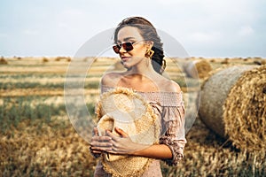 Smiling woman in sunglasses with bare shoulders on a background of wheat field and bales of hay