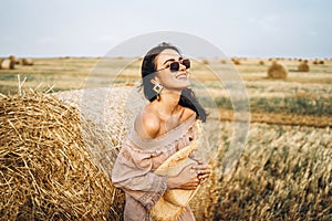 Smiling woman in sunglasses with bare shoulders on a background of wheat field and bales of hay