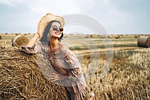 Smiling woman in sunglasses with bare shoulders on a background of wheat field and bales of hay