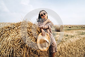 Smiling woman in sunglasses with bare shoulders on a background of wheat field and bales of hay