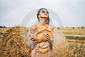 Smiling woman in sunglasses with bare shoulders on a background of wheat field and bales of hay