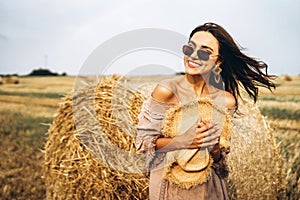 Smiling woman in sunglasses with bare shoulders on a background of wheat field and bales of hay