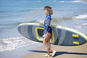 Smiling woman with SUP board on seashore at daylight