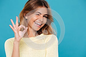 Smiling woman in sweater showing ok sign and winks