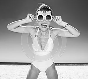Smiling woman in swimsuit and funky pineapple glasses at beach