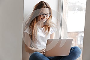 Smiling woman in t-shirt and eyeglasses sitting on windowsill