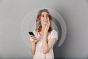 Smiling woman in t-shirt holding smartphone and looking away