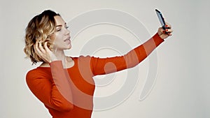 Smiling woman taking self portrait on smart phone, over grey background