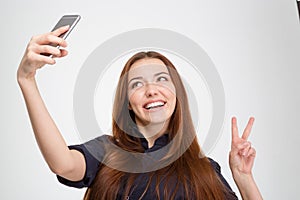 Smiling woman taking selfie with mobile phone showing victory sign