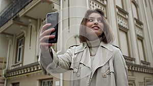 Smiling woman taking selfie on urban street. Girl pouting lips for phone camera.