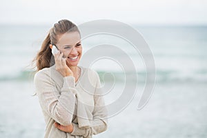 Smiling woman talking cell phone on cold beach