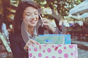 Smiling woman talking phone, looking in shopping bags.