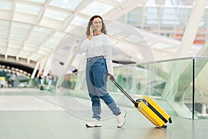 Smiling Woman Talking on Phone While Walking With Suitcase at Airport Terminal