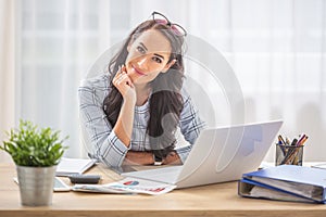 Smiling woman with titled head leaned on her hand sitting at her office desk