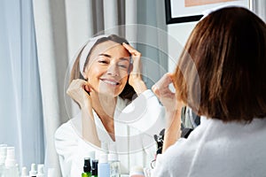 Smiling woman touching face wearing housecoat before mirror photo