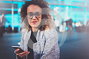 Smiling woman tourist wearing eye glasses and searching way in navigation map by cell telephone, while is standing on